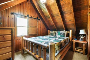 A wooden cabin bedroom with a bed, a nightstand, a lamp, and a window.