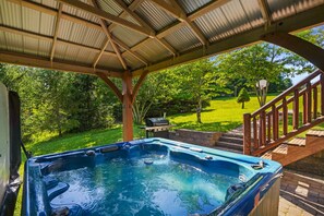 Un bain à remous installé sous une terrasse couverte, avec vue sur une pelouse et un escalier en bois.