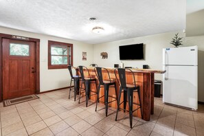 A kitchen with a wooden island, bar stools, a refrigerator, and a television mounted on the wall.