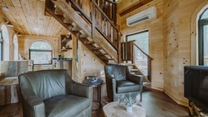L’intérieur d’un chalet en bois comprend un escalier, des fauteuils en cuir, une petite table et un téléviseur.