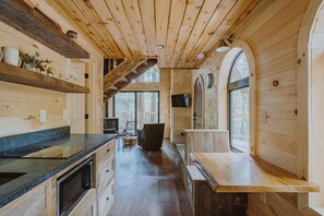 Interior de una cabaña de madera con cocina, una mesa de comedor y un ventanal grande.