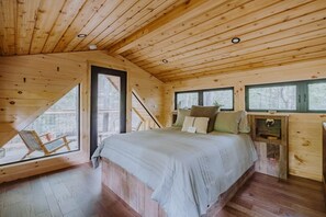 Un dormitorio de cabaña de madera con una cama, una ventana y una mesita.