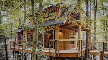 A wooden treehouse with multiple levels, built into a forested area.