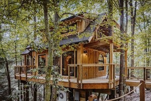 A wooden treehouse with multiple levels, built into a forested area. - The Hickory Treehouse w/ Suspension Bridge (South Bloomingville)