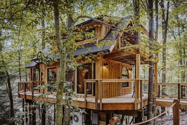 A wooden treehouse with multiple levels, built into a forested area.