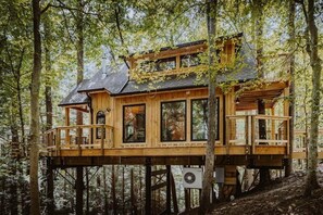 A wooden treehouse with multiple levels, built on stilts in a forest. - The Hickory Treehouse w/ Suspension Bridge (South Bloomingville)