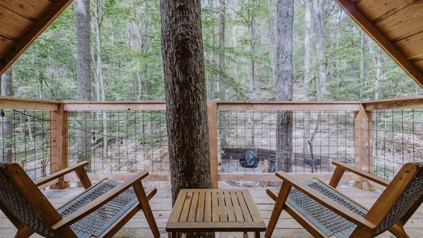 Une terrasse en bois avec deux chaises et une table, entourée d’une clôture en métal, donnant sur une zone boisée.