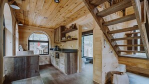Un intérieur en bois comprenant un espace cuisine, un escalier en bois et une grande fenêtre en arc de cercle.
