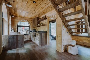 A wooden interior with a kitchen area, wooden staircase, and a large arched window. - The Hickory Treehouse w/ Suspension Bridge (South Bloomingville)