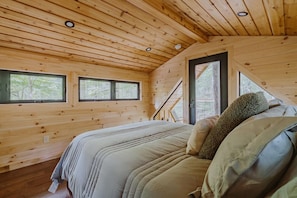 A wooden cabin bedroom with a bed, two windows, and a door. - The Hickory Treehouse w/ Suspension Bridge (South Bloomingville)