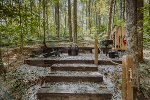 A rustic outdoor cabin with a fire pit, wooden benches, and a small shed with a fire extinguisher. - The Tulip Treehouse | Hocking Hills (South Bloomingville)
