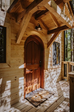 Une cabane en bois dotée d’une grande porte en arc de cercle, d’une fenêtre et d’un porche.