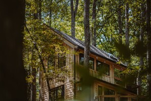 Une cabane en bois dotée d’un balcon, entourée de grands arbres et surplombant un ciel dégagé.