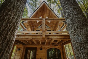 A wooden cabin with a balcony, surrounded by trees.