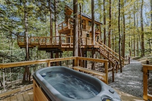 Eine Holzhütte mit Whirlpool und Terrasse, umgeben von Bäumen.