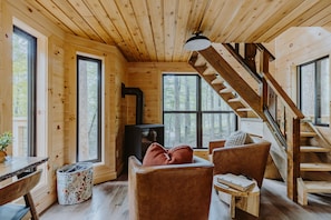 L’intérieur d’un chalet en bois, avec un escalier, de grandes fenêtres, une cheminée et un coin salon confortable.