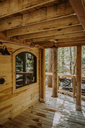 A wooden cabin interior with a large arched window, wooden beams, and a wooden deck.