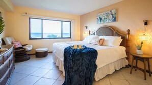 A bedroom with a large bed, a window with a view, a bedside table with a lamp, and a chair.
