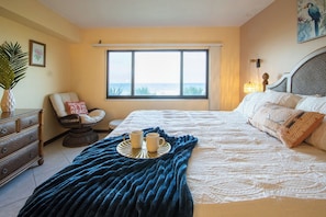 Un dormitorio con una cama grande, una silla, un tocador, una ventana con vistas y un cojín decorativo.