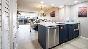 A modern kitchen with a central island, stainless steel appliances, and a view to the balcony. - Beachside Bliss | Ocean View Condo w/ Heated Pool, Spa & Direct Beach Access 🌴 (Cape Canaveral)