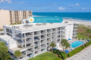 A multi-story hotel with balconies, a pool, and a view of the beach.