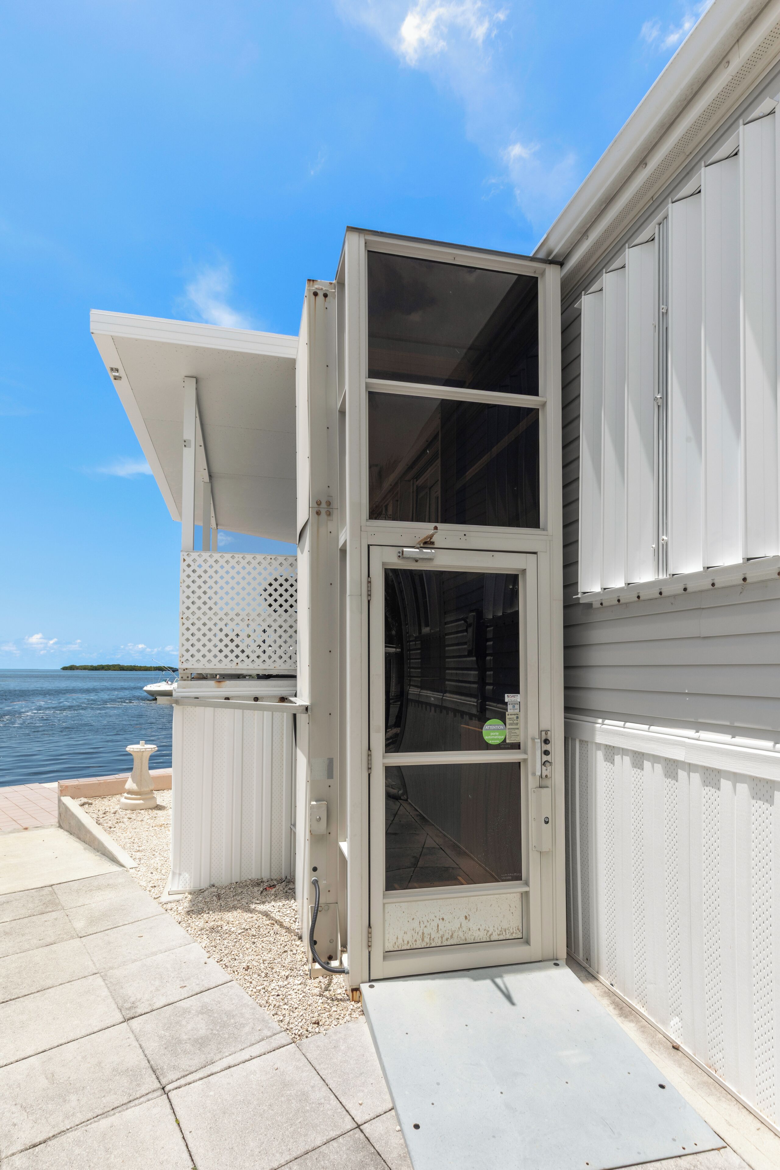 A coastal building with a sliding glass door, a covered porch, and a view of the sea.