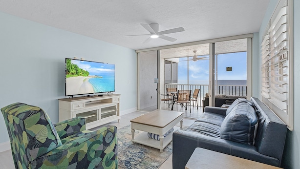 A living room with a television, a sofa, a coffee table, and a patterned armchair.