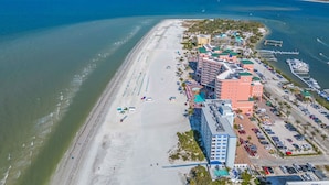 An aerial view of a coastal hotel with a beach, parking area, and marina.