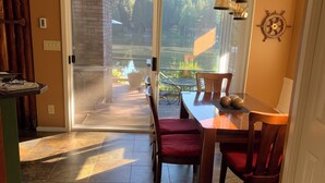 Un coin repas avec une table et des chaises, une vue sur un jardin par une porte vitrée et une décoration murale représentant un gouvernail de bateau.