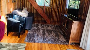 Une pièce chaleureuse avec des murs en bois, un canapé en cuir noir, un téléviseur et un meuble en bois.