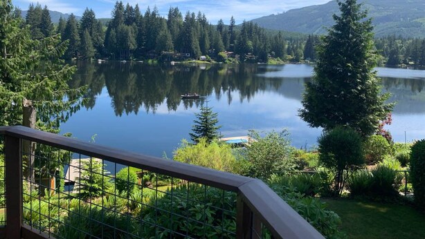 Un lac paisible, entouré d’une forêt dense et de montagnes, sous un ciel dégagé.