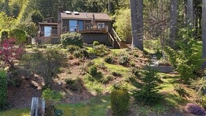 Une maison entourée d’un jardin aménagé, avec un mur en pierre et une terrasse en bois.