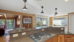 Une cuisine moderne dotée de plans de travail en granit, d’une cuisinière à gaz, d’armoires en bois et de luminaires suspendus.