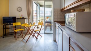 Una cocina compacta con refrigerador, una mesa de comedor con sillas, un televisor y un reloj en la pared.