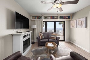 A living room with a fireplace, a flat-screen TV, a leather sofa, and a view of the ocean through large windows.