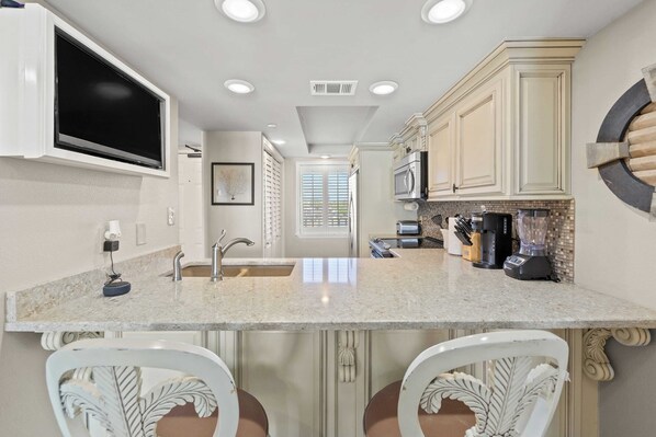 A kitchen with a granite countertop, white cabinetry, a built-in microwave, and a blender.