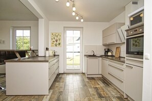 Eine moderne Küche mit weißen Schränken, einer zentralen Kochinsel und einem großen Fenster.