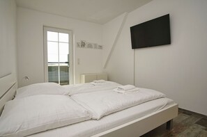 Et soveværelse med seng, fjernsyn ophængt på væggen og dør til en balkon.