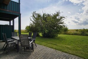 An outdoor patio with a table and chairs, surrounded by a grassy area and a large bush. - Haus in Idyllischer Lage mit Terrasse und Garten - Villa Vogelblick Haus 01 - Villa Vogelblick (Trent)