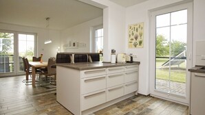 A modern kitchen with a central island, white cabinetry, and a large window providing a view of the outdoors.
