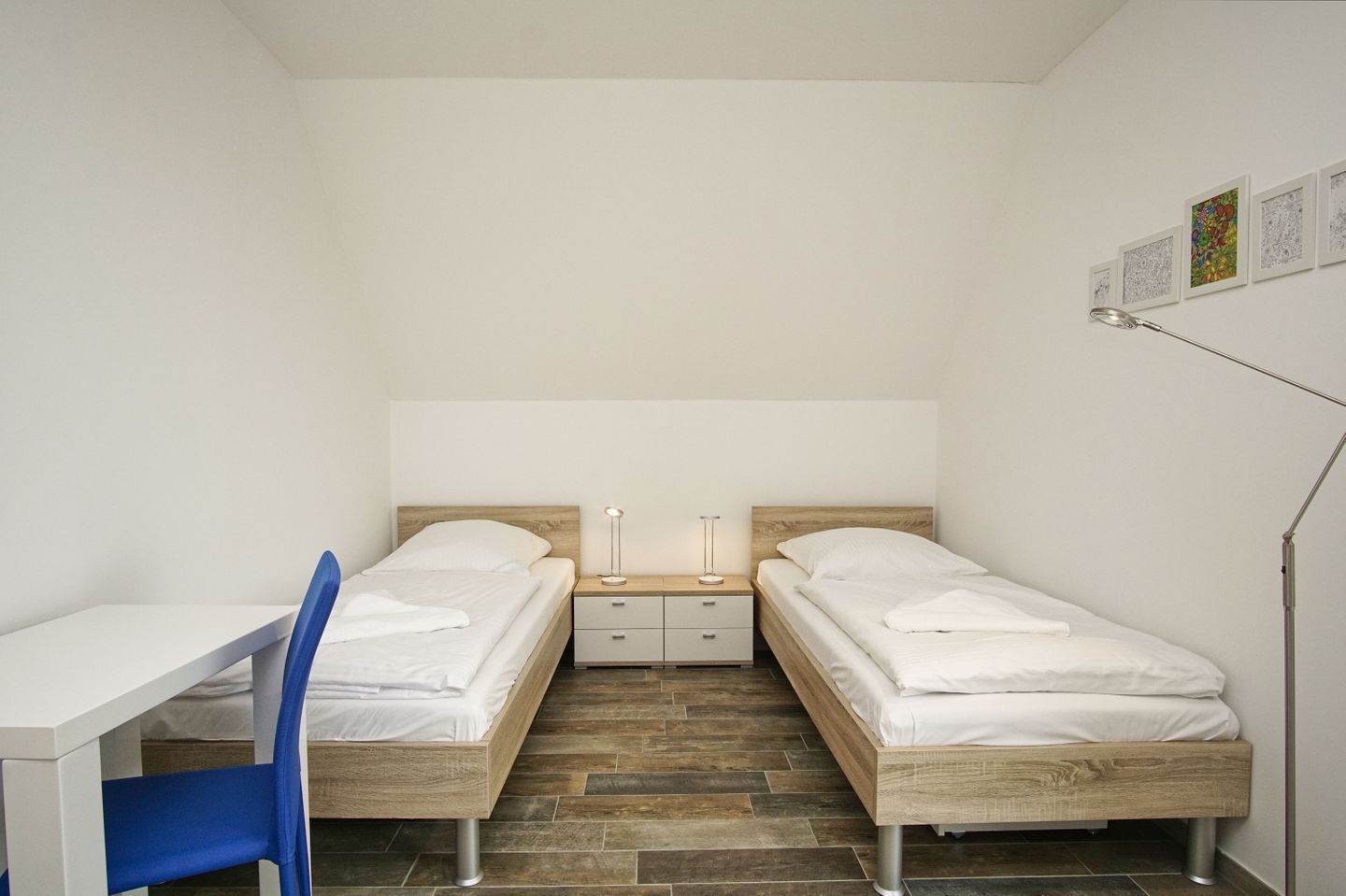 Ein kleines, modernes Schlafzimmer mit zwei Einzelbetten, einem Schreibtisch und einem Stuhl.