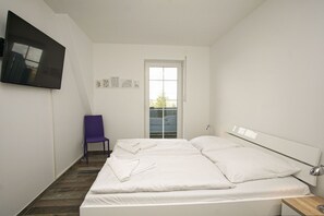 Ein Schlafzimmer mit Bett, Sessel, Fernseher und Fenster.