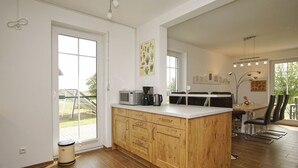 Cocina moderna con armarios de madera, microondas integrado y cafetera. Hay un comedor con mesa y sillas, y un ventanal que proporciona luz natural.