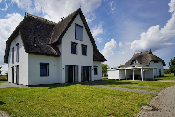 A two-story house with a thatched roof, a covered porch, and a well-maintained lawn.