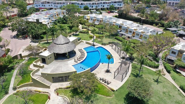 Vue aérienne d’un complexe hôtelier doté d’une piscine centrale, d’un pavillon à toit de chaume et de plusieurs bâtiments d’hôtel.