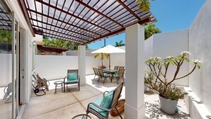Une terrasse avec une table et des chaises, une pergola et un pot de fleurs.