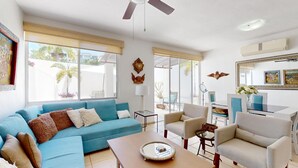 Un salon spacieux avec un canapé bleu, des fauteuils beige, une table basse et un coin repas comprenant une table et des chaises en verre.