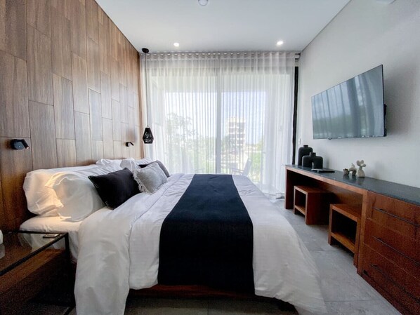 Ein modernes Schlafzimmer mit einem großen Bett, einem hölzernen Kopfteil, einem an der Wand montierten Fernseher und einem Schreibtisch mit Schubladen.