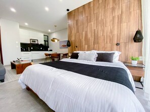 Ein modernes Schlafzimmer mit einem großen Bett, einer Wand in Holzoptik und einer Küchenzeile im Hintergrund.