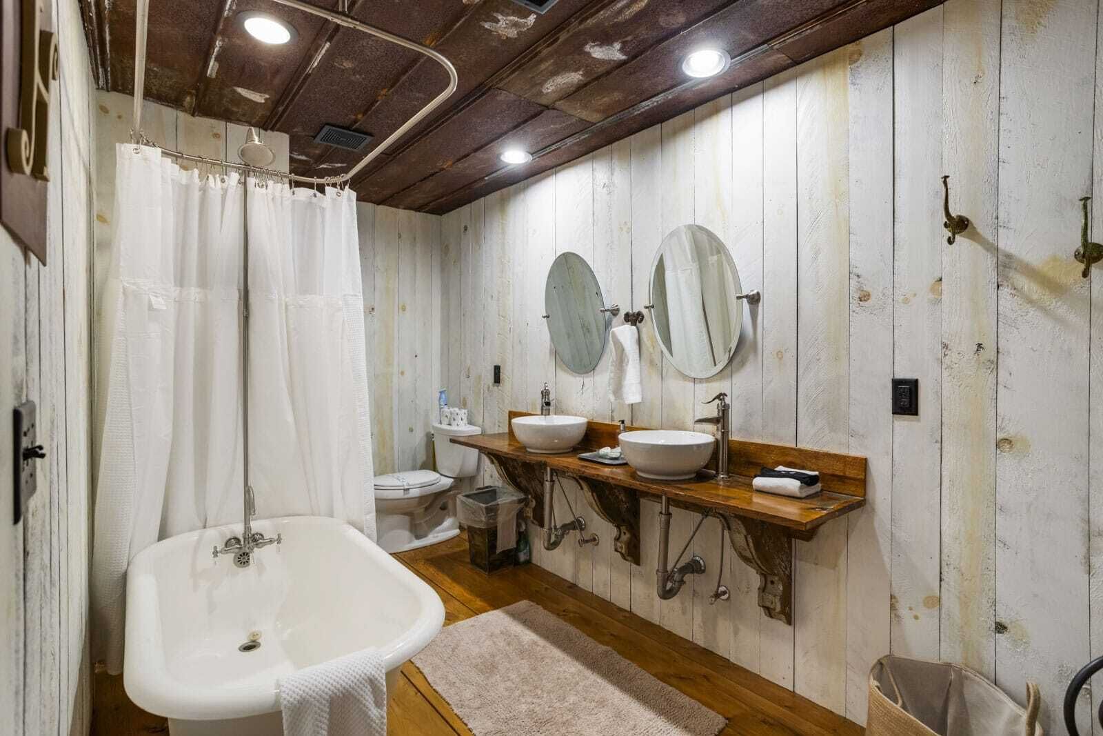 Ein rustikales Badezimmer mit Badewanne, zwei Waschbecken und einer Duschvorhang.